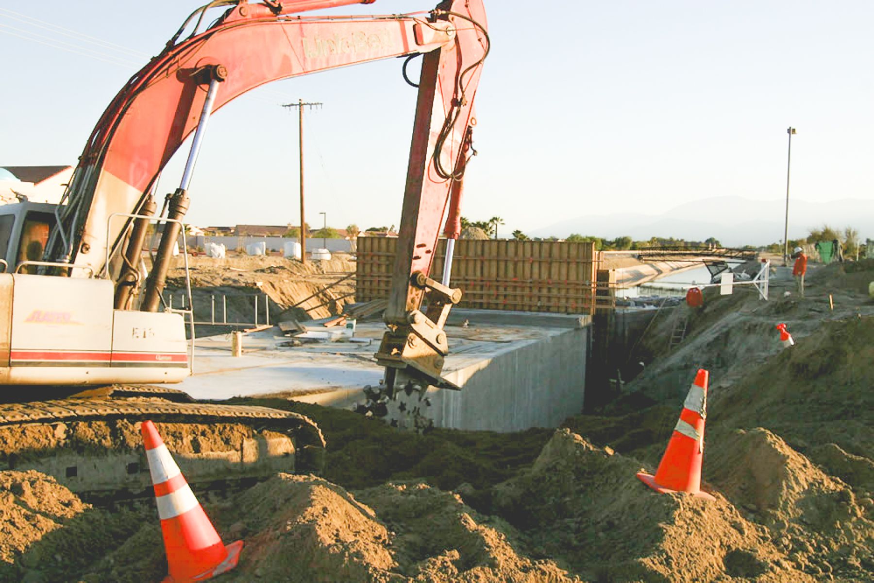 Red tracked excavator digging beside the poured concrete slab, with cones on the spoil piles