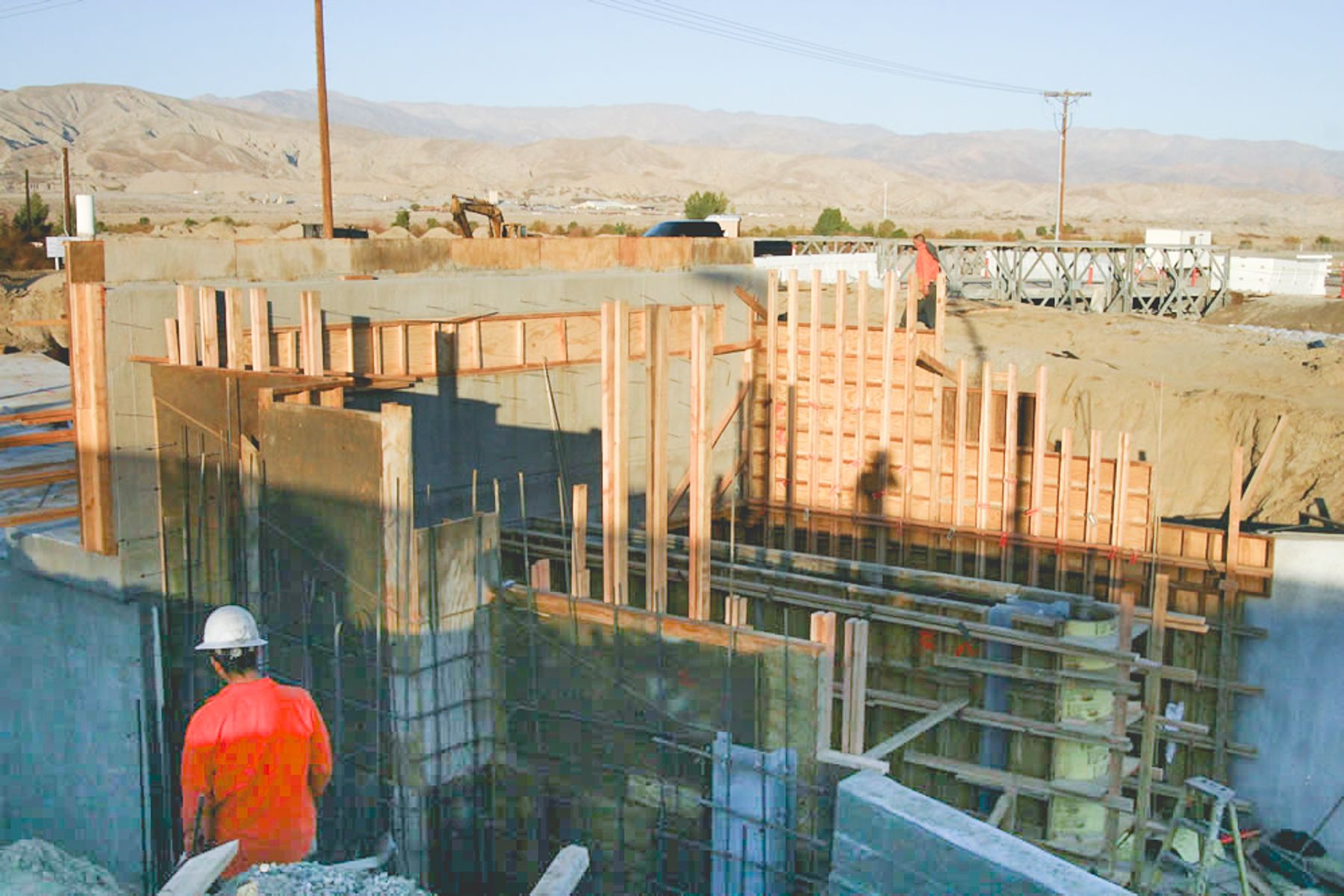 Worker in orange hi-vis and a white hard hat looking over formed walls and reinforcing steel inside the structure