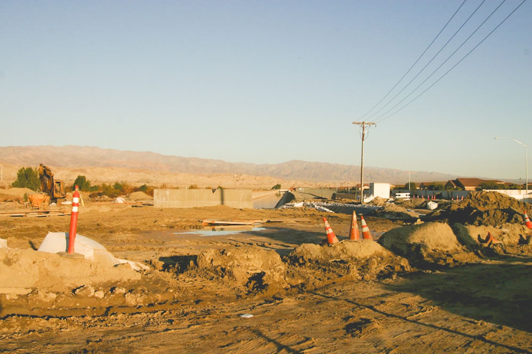 Site overview at golden hour, with cones, spoil piles, standing water and the concrete structure in the distance
